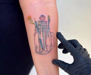 קעקוע של מברשות צבע ופרח בתוך כוס ביצוע של בוגרת קורס קעקועים מקיף של TATTOOTLV