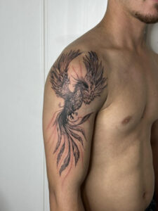 קעקוע של פניקס שחור לבן על הזרוע העליונה החיצונית