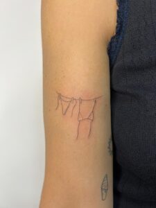 קעקוע של קו אחד של הלבשה תחתונה על חבל כביסה ביצוע של בוגרת קורס קעקועים פיין ליין TATTOOTLV