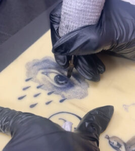 מכונת קעקועים מקעקעת עין במסגרת קורס קעקועים אקדמיית מאמא אינק